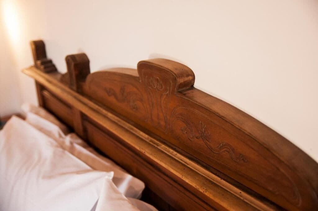 A wooden headboard with carved designs, a white bedspread, and a bedside lamp.