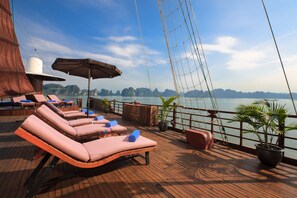 Eine Terrasse mit Liegestühlen, einem großen Sonnenschirm und Blumentöpfen.