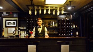A bar area with a bartender, shelves of liquor bottles, and bar stools. - Halong Glory Legend Cruise (Tuan Chau)