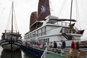A ferry with a white upper deck and a black lower deck, passengers boarding and disembarking. - Halong Glory Legend Cruise (Tuan Chau)
