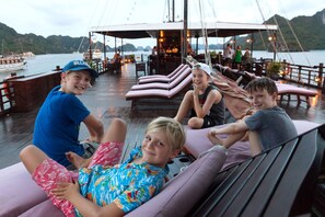 En gruppe mennesker slapper af på en bådterrasse med liggestole, og der er et spiseområde i baggrunden.