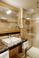 Un baño moderno con un espejo grande, un lavabo blanco, una ducha con cerramiento de vidrio y una encimera de mármol.
