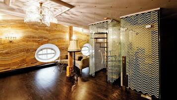 Quarto com piso de madeira, um lustre, uma janela redonda e um espelho com padrão em zigue-zague.
