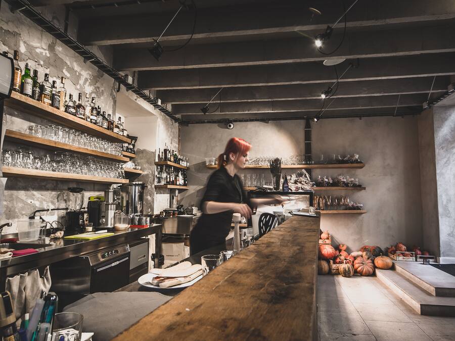 A kitchen with shelves of bottles and glasses, a wooden counter, and pumpkins on the floor.
