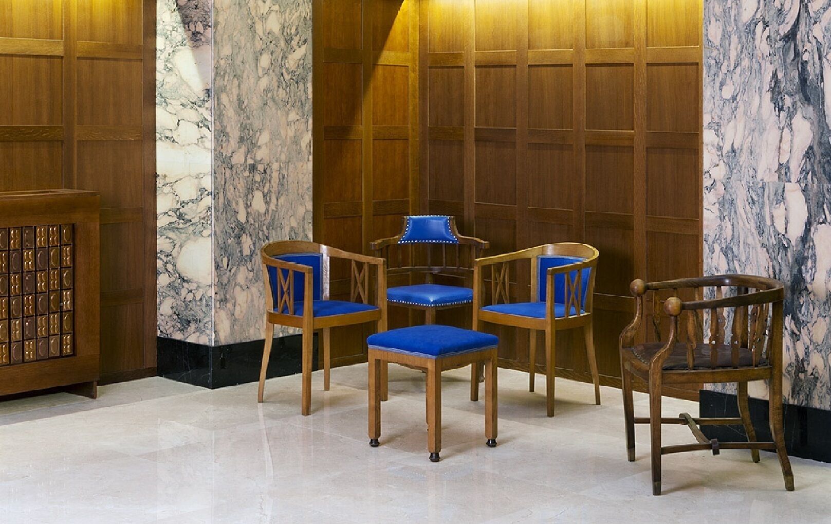 A room with a marble wall, wooden paneling, and a small table with four blue chairs.