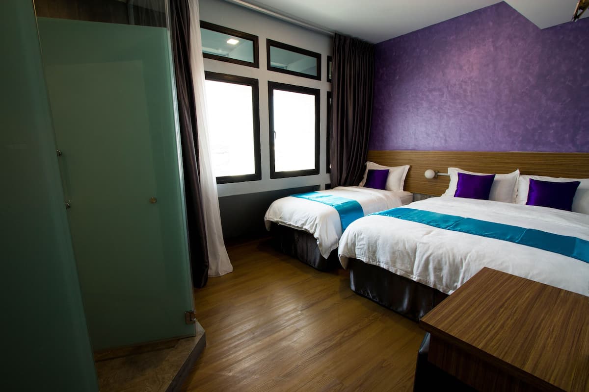 Een hotelkamer met twee bedden, een houten hoofdbord, een raam met gordijnen en een houten vloer.