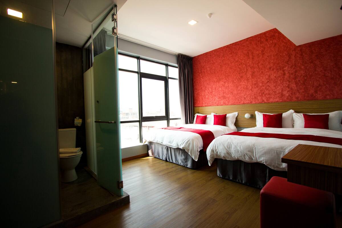 Een hotelkamer met twee bedden, een houten vloer, een rode wand en een raam met gordijnen.