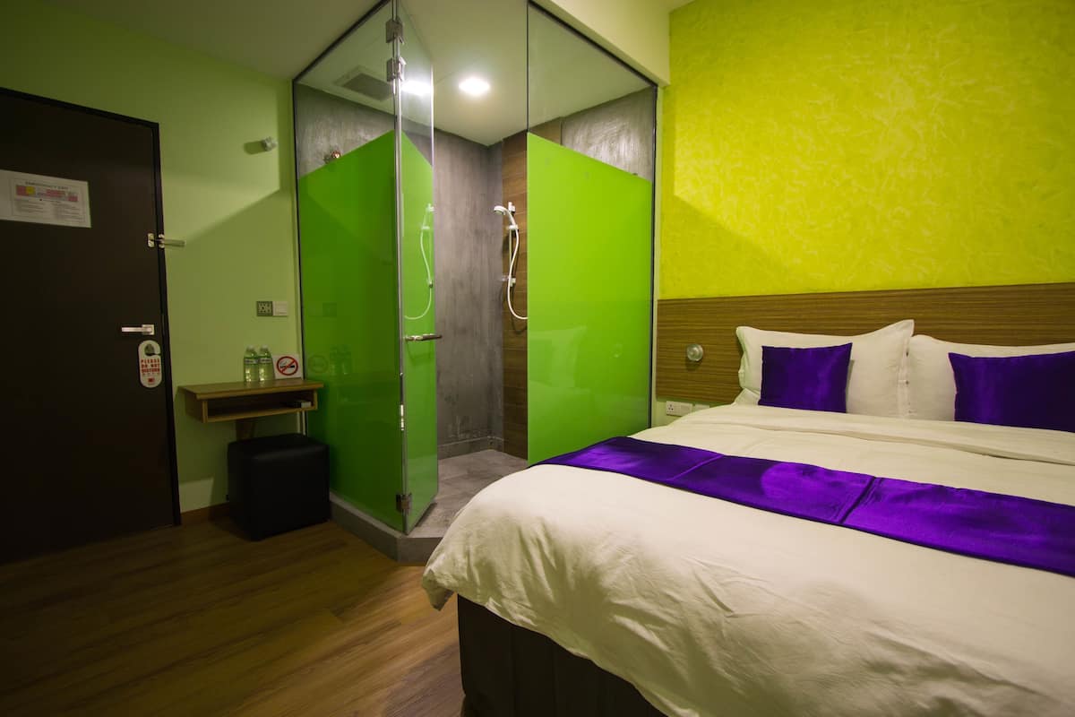 Een hotelkamer met een bed, een douche en een houten vloer.