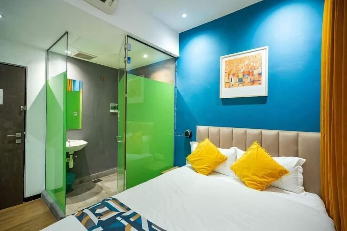 Een hotelkamer met een bed, een badkamer met glazen scheidingswand en een blauwe accentmuur.
