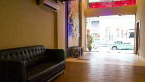 A lobby with a dark leather sofa, wooden flooring, a large abstract painting, and a view of the street through the entrance.