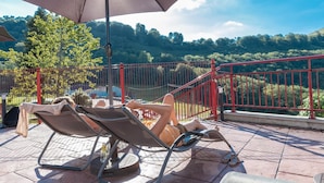 A terrace with two lounge chairs and a large umbrella, overlooking a scenic hillside. - Hôtel et Restaurant du Col Osquich (Musculdy)