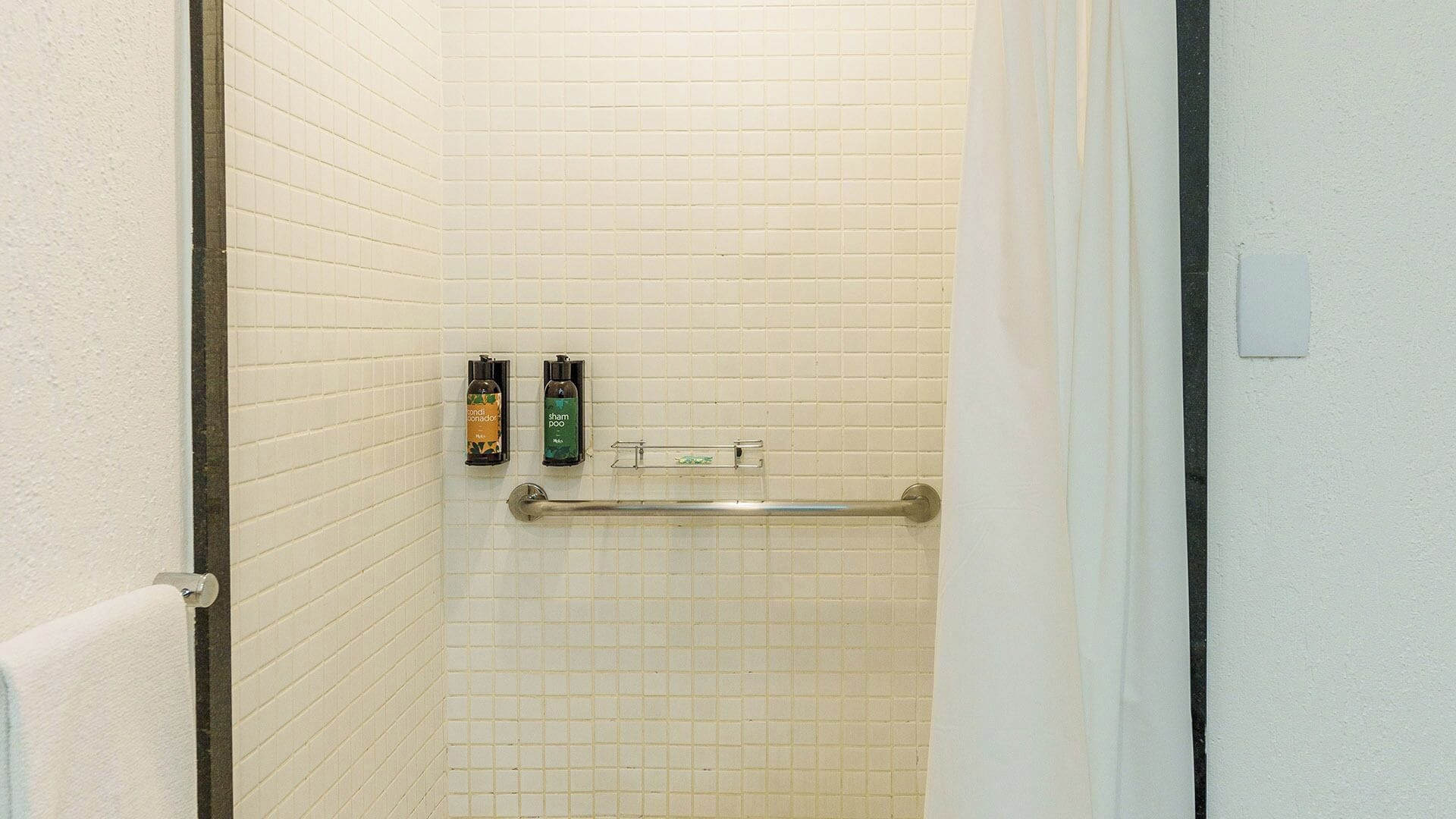 Une salle de bain avec des murs carrelés de carreaux blancs, un porte-serviettes et deux articles de toilette accrochés au mur.