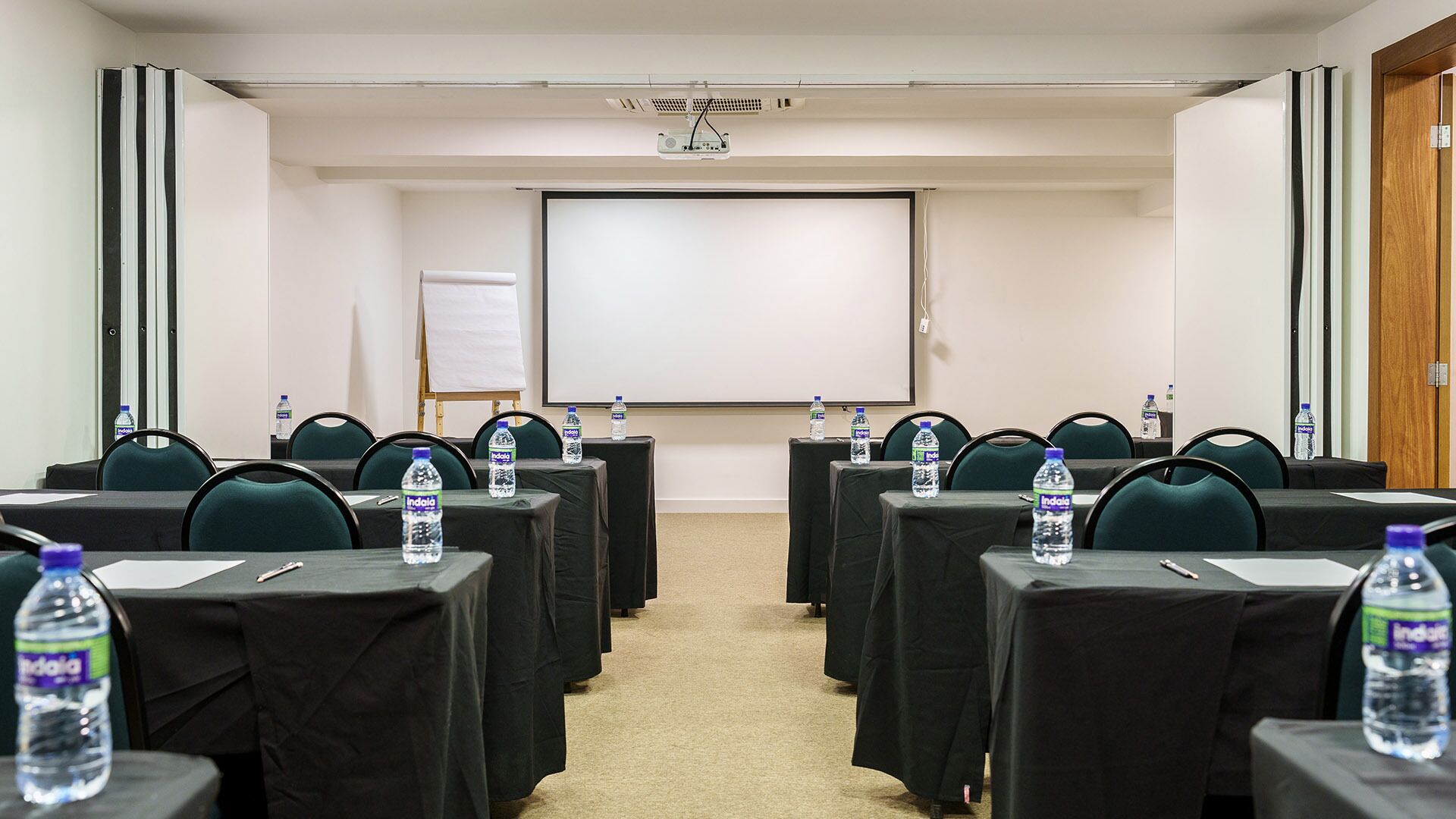 Un salón de conferencias con filas de mesas, sillas y botellas de agua.