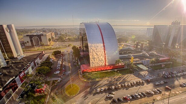 A modern building with a curved glass facade, surrounded by parking lots and other urban structures. - Athos Bulcão Hplus Executive (Brasília)