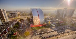 Un edificio moderno con fachada de vidrio curvada, rodeado de estacionamientos y otras construcciones urbanas.