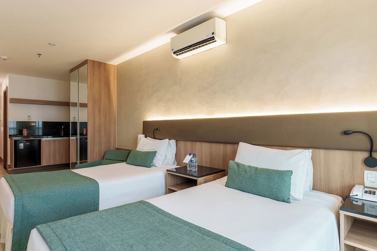 A hotel room with two beds, a desk, a chair, a minibar, and a bathroom.