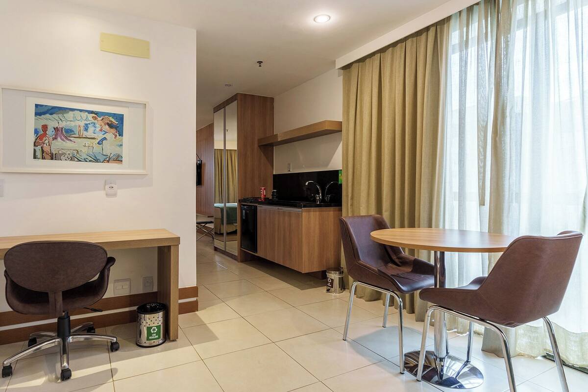 A hotel room with a kitchenette, a dining area with two chairs, a small table, and a painting on the wall.