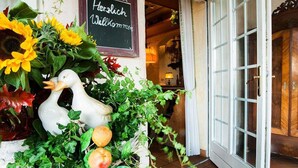 A hotel entrance with a welcome sign, a white duck decoration, and a variety of plants. - Hotel Restaurant Jagdhof (Steinhagen)
