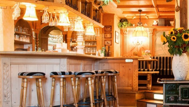 A rustic interior with wooden bar stools, a vintage stove, and a vase with sunflowers. - Hotel Restaurant Jagdhof (Steinhagen)