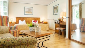 A hotel room with a bed, two bedside tables with lamps, a wooden desk with a chair, a sofa, and a small table with decorative items. - Hotel Restaurant Jagdhof (Steinhagen)
