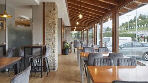 A restaurant with wooden tables and chairs, stone walls, and large windows offering a view of the street. - Hotel Iriguibel (Huarte)
