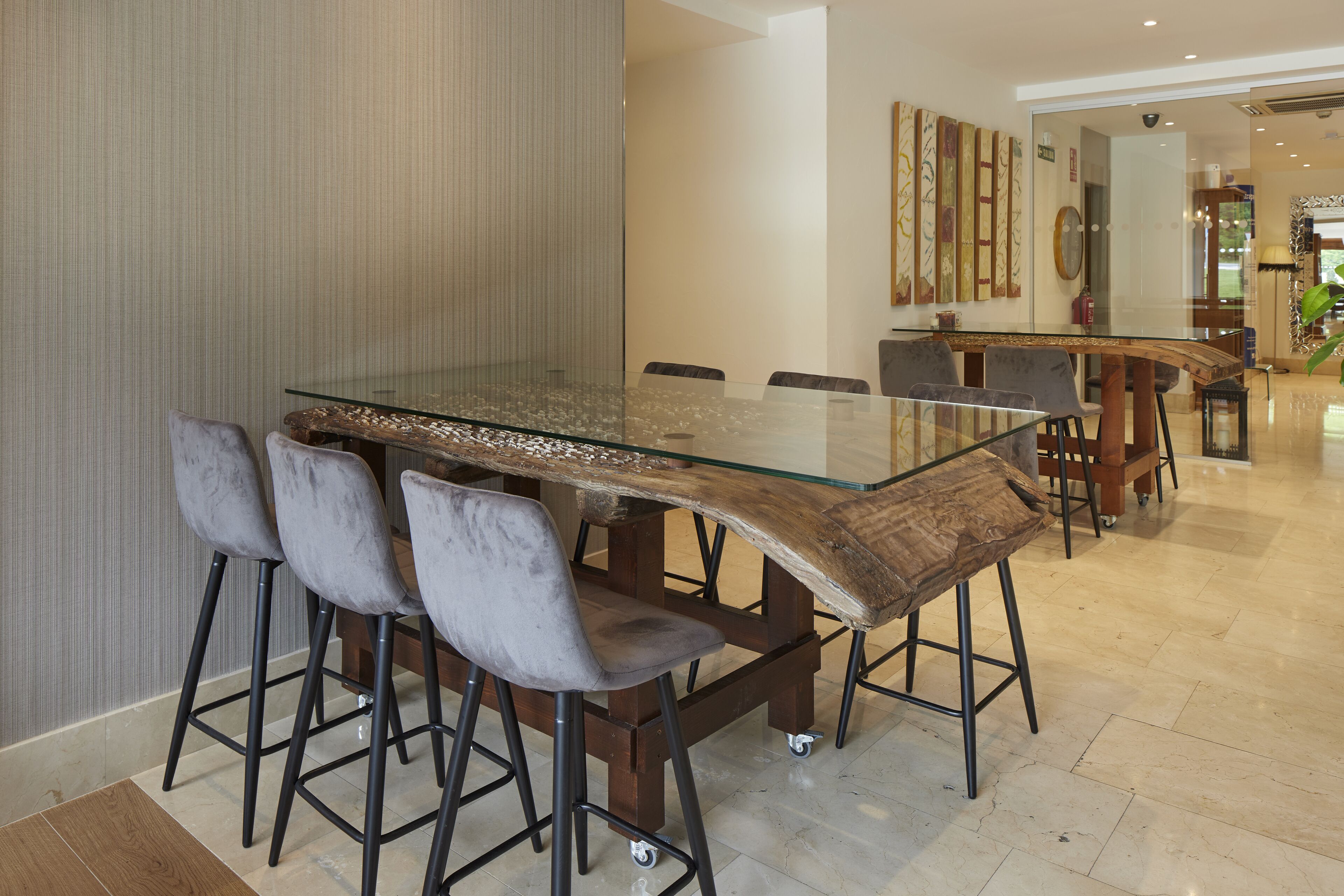 A modern dining area with a glass-top table, bar stools, and a wooden accent.