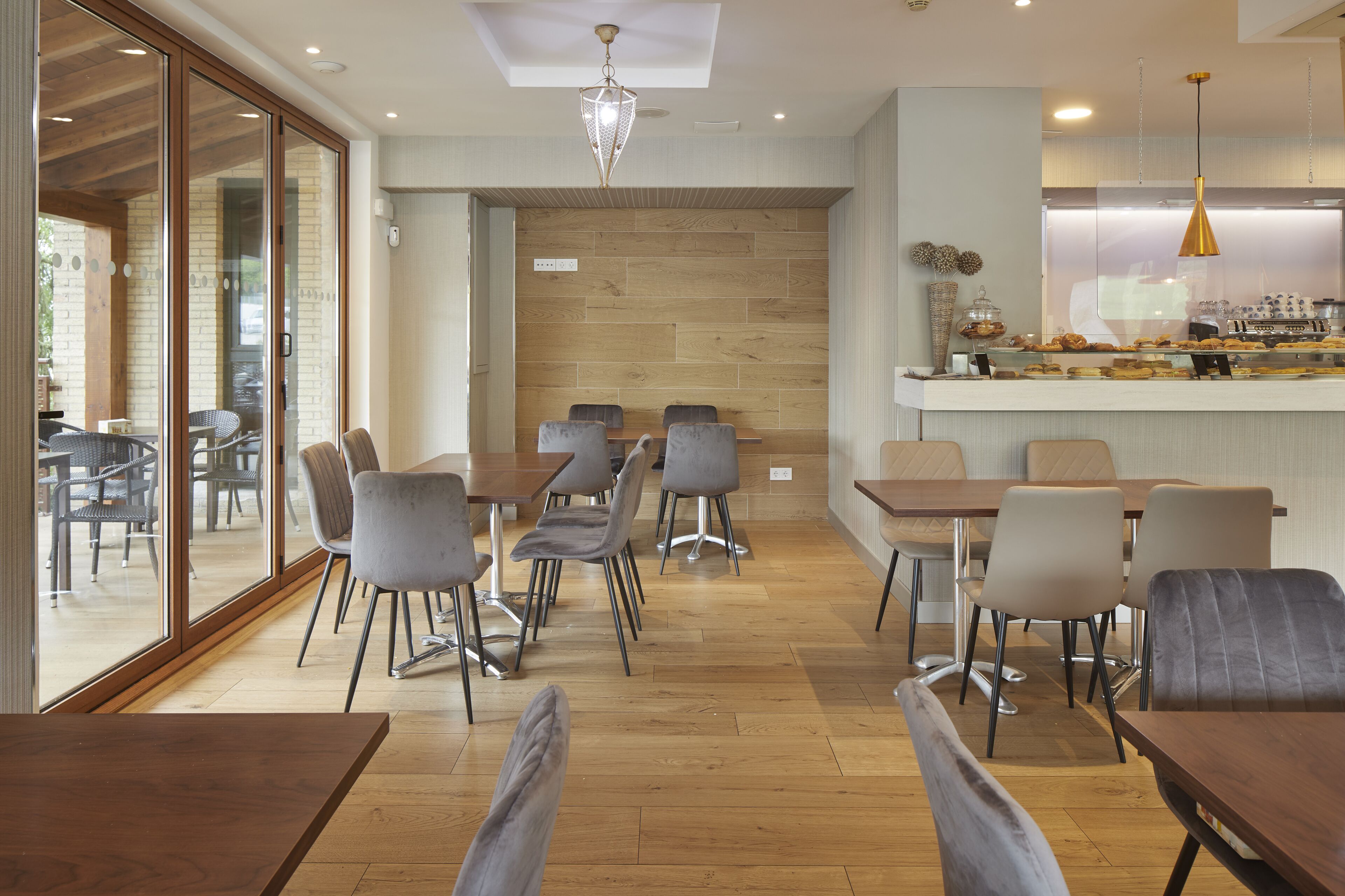 Una cafetería moderna con piso de madera, sillas tapizadas en gris y una mesa de madera en el centro.