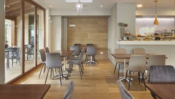 Una cafetería moderna con piso de madera, sillas tapizadas en gris y una mesa de madera en el centro.
