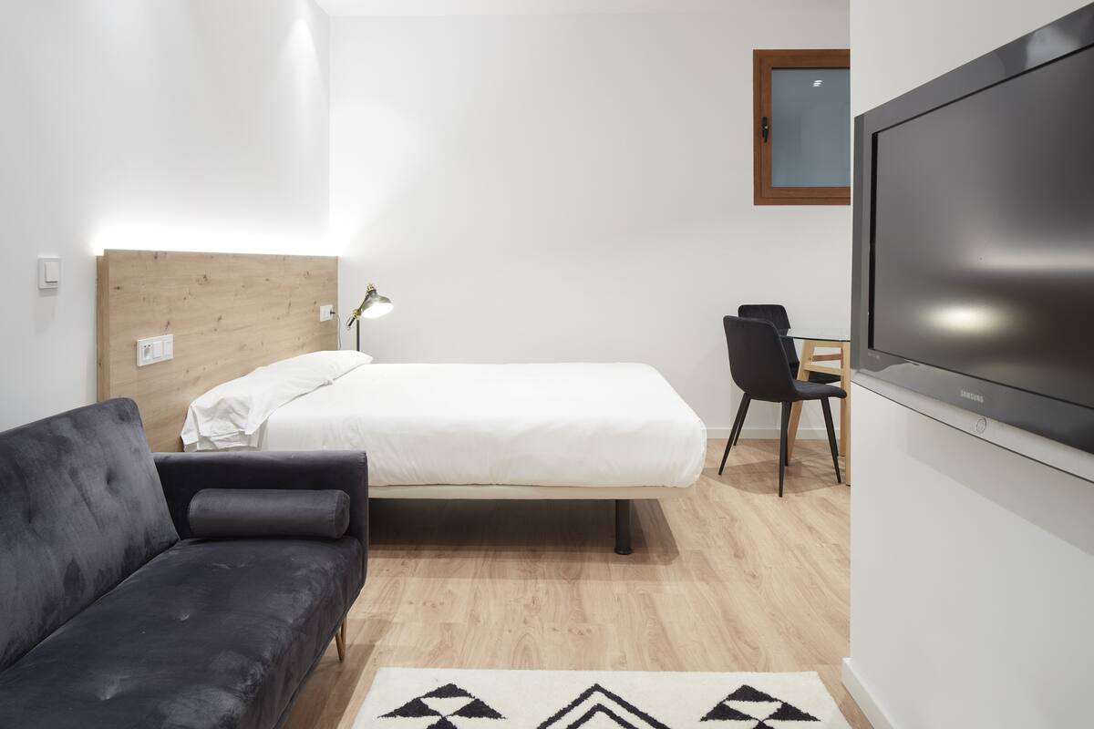 A modern hotel room with a bed, a sofa, a desk, and a TV.
