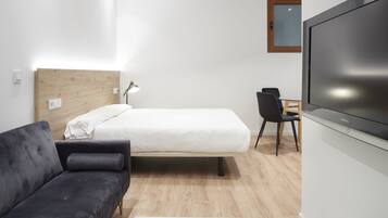 A modern hotel room with a bed, a sofa, a desk, and a TV.