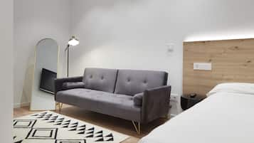 A modern bedroom with a grey sofa, a white bed, a patterned rug, a floor lamp, and a wooden headboard.