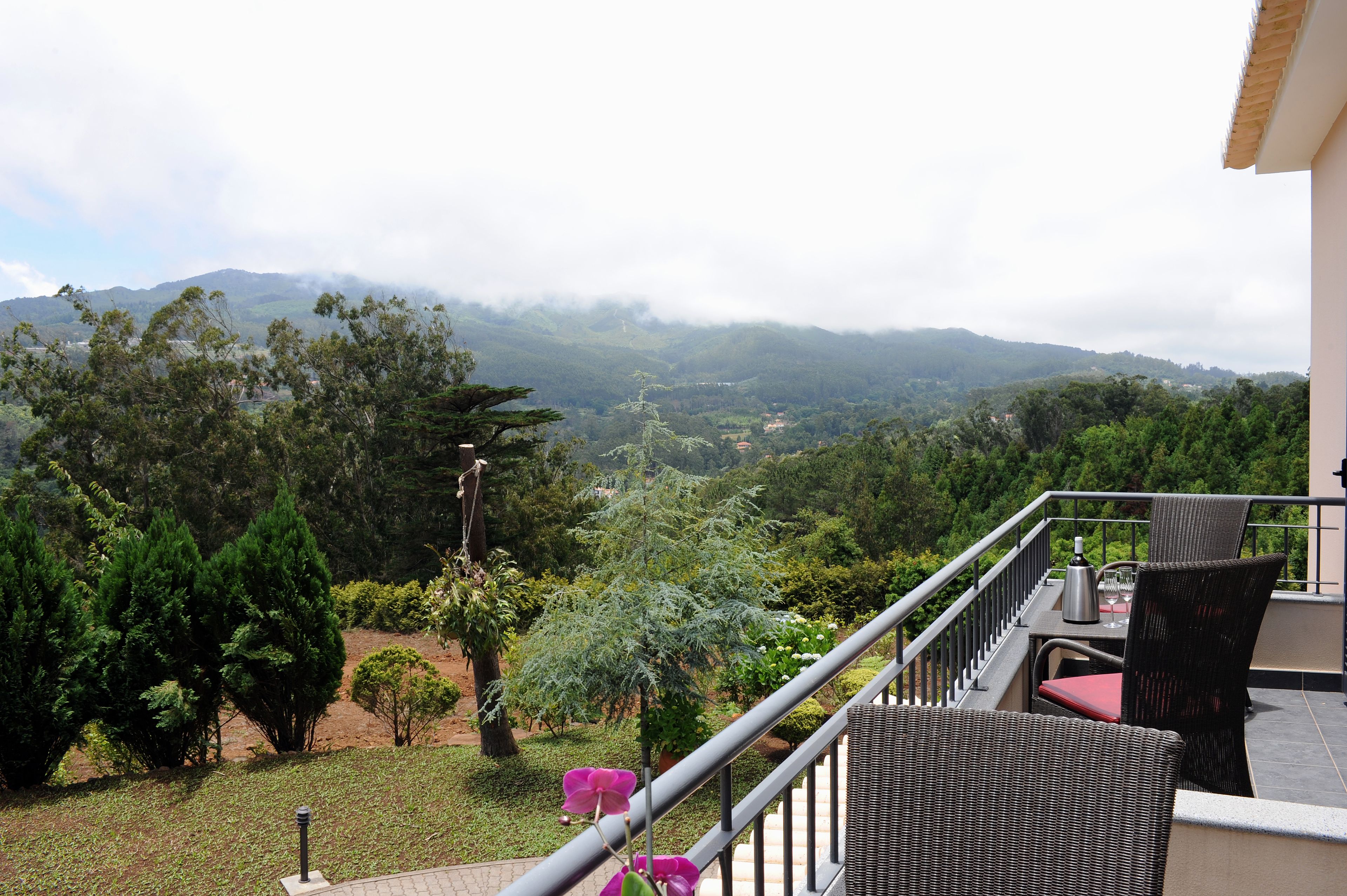A balcony with wicker furniture, a view of a lush landscape with trees and mountains, and a clear sky.