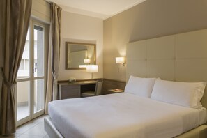 Habitación de hotel con una cama grande, un escritorio, una silla, un espejo y una ventana con cortinas.