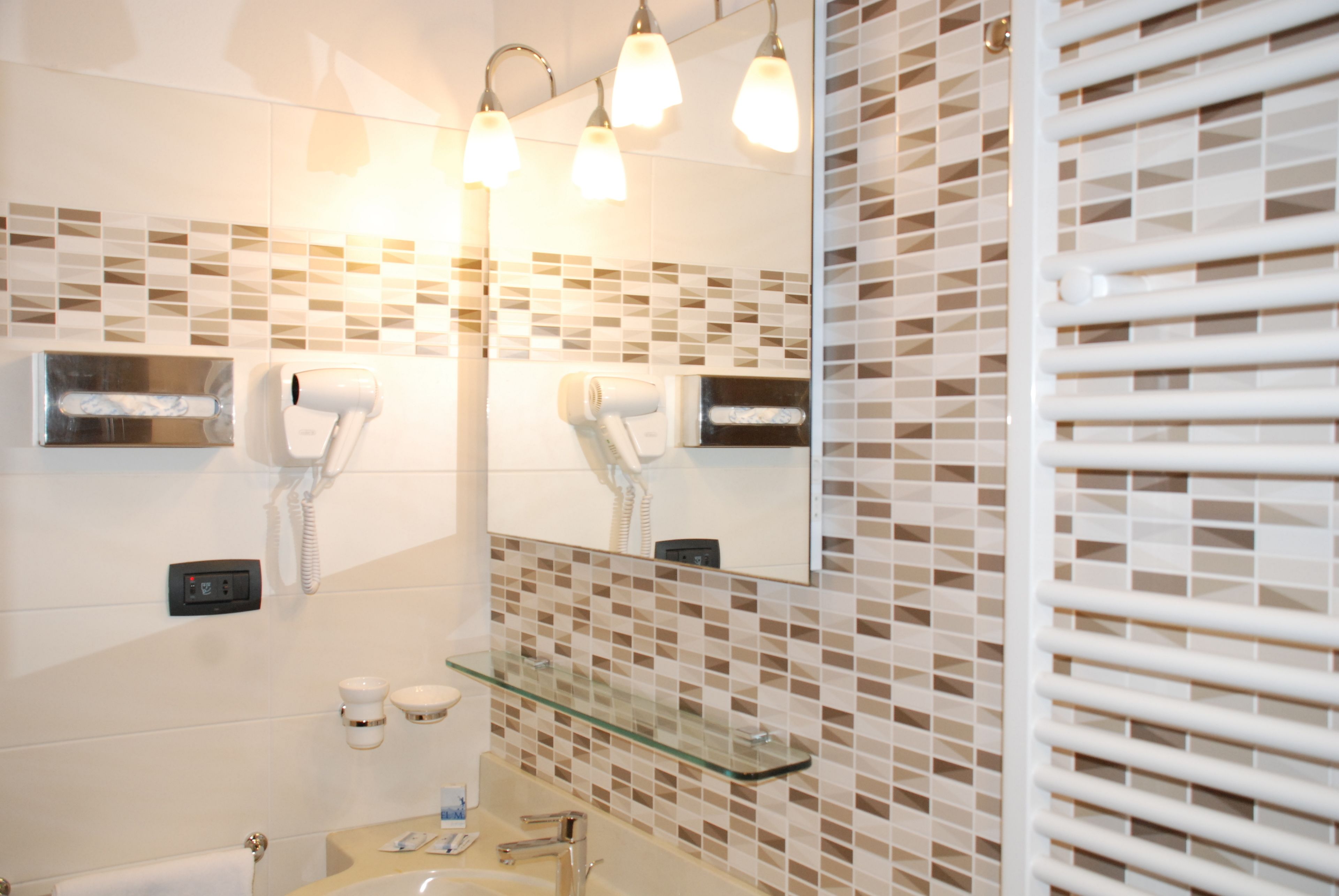 A modern bathroom with a glass shelf, two hair dryers, and a mirror.