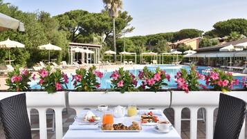 A poolside dining area with a table set for breakfast, overlooking a swimming pool.