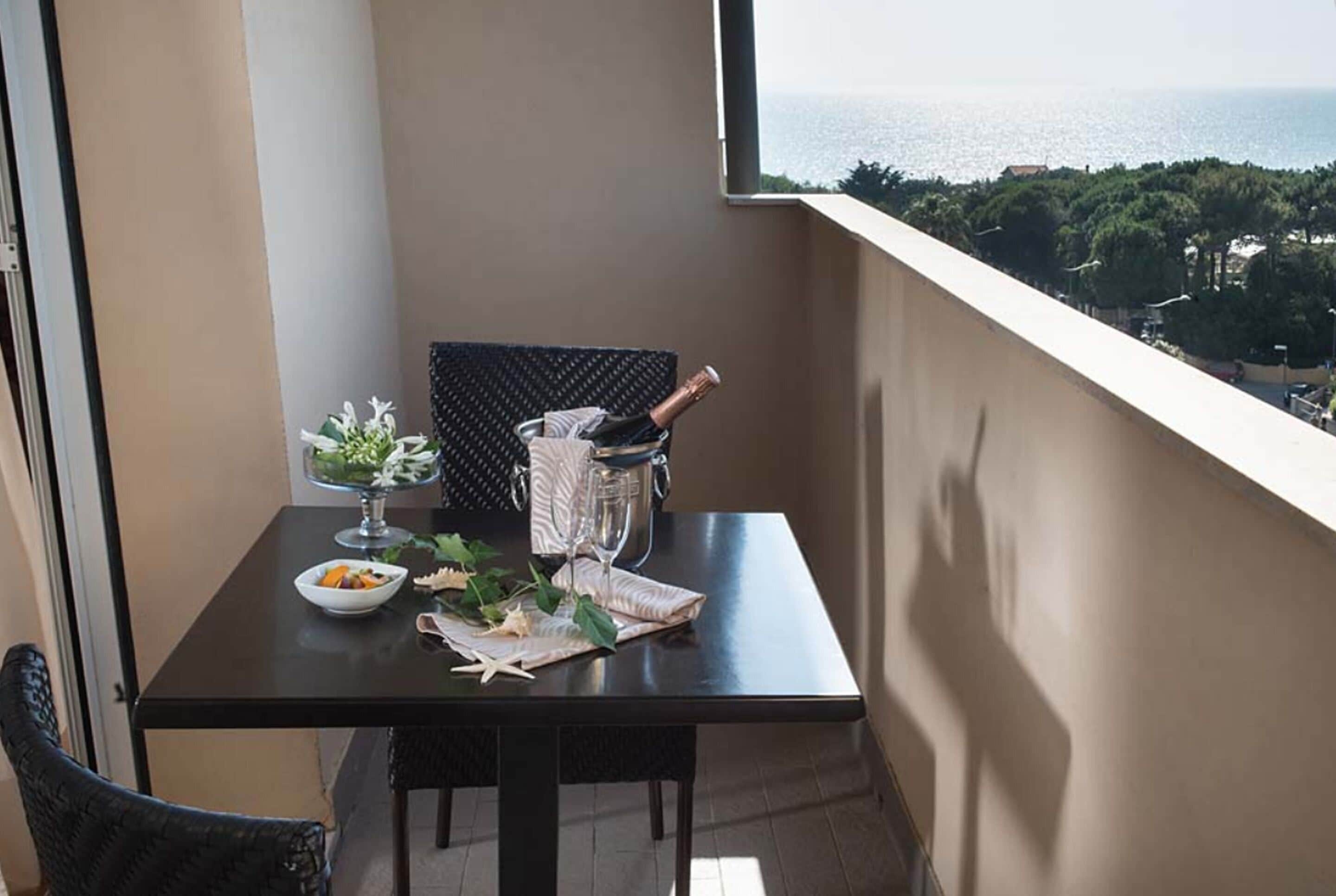Un balcon avec une table dressée pour le dîner, une bouteille de champagne et une vue sur la mer.