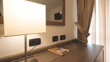 Ein Hotelzimmer mit einem Holztisch, einer Lampe, einem Spiegel, einem Telefon und einem Fenster mit Vorhängen.