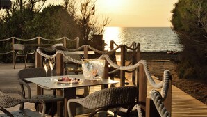 Un área de comedor al aire libre con sillas y mesas de mimbre, con vista al mar.