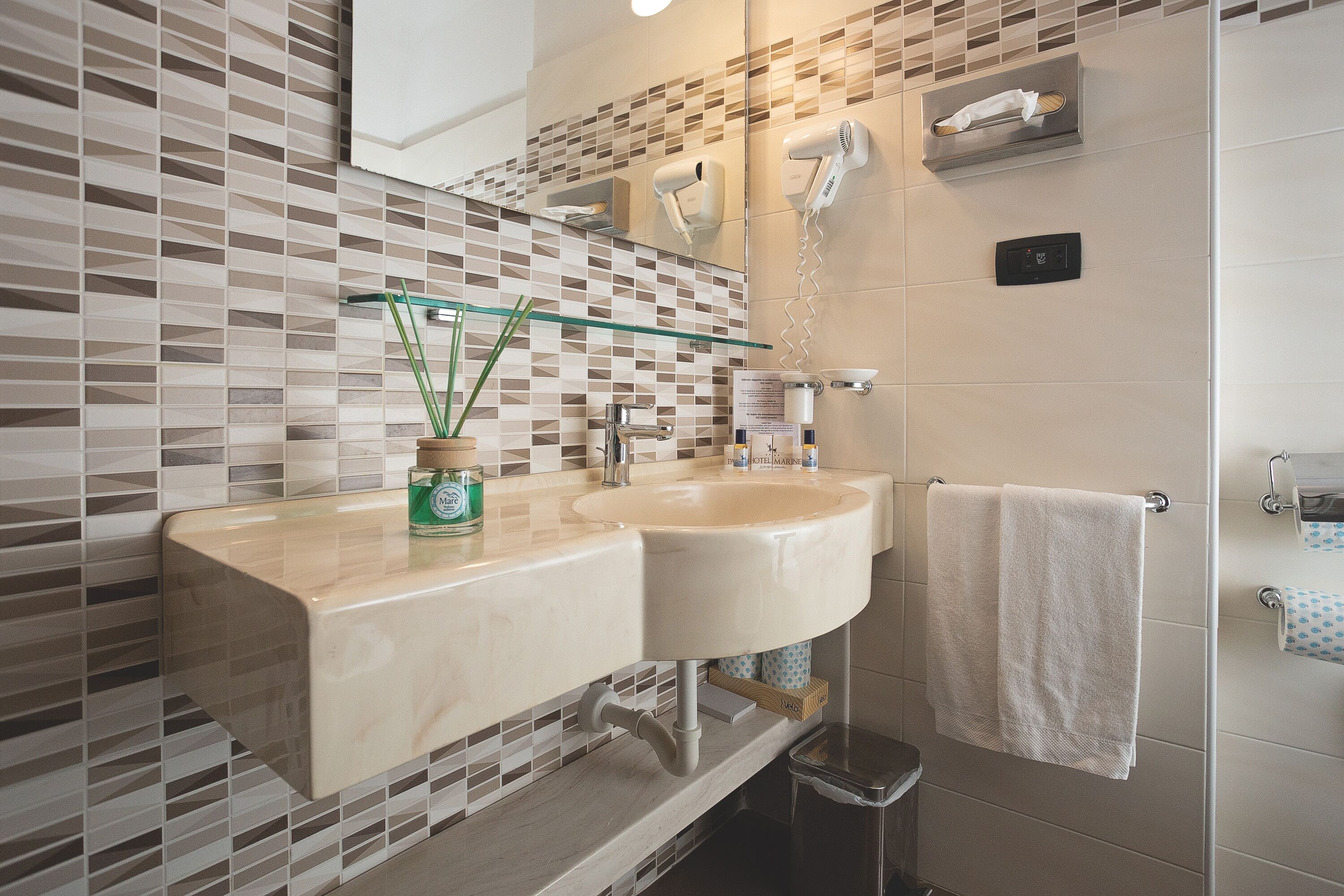 Un bagno con doppio lavabo, una mensola in vetro con una pianta, un portasciugamani e un asciugacapelli a parete.