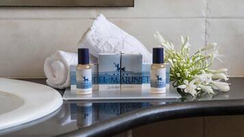 A bathroom counter with toiletries, a rolled towel, and a vase of white flowers.