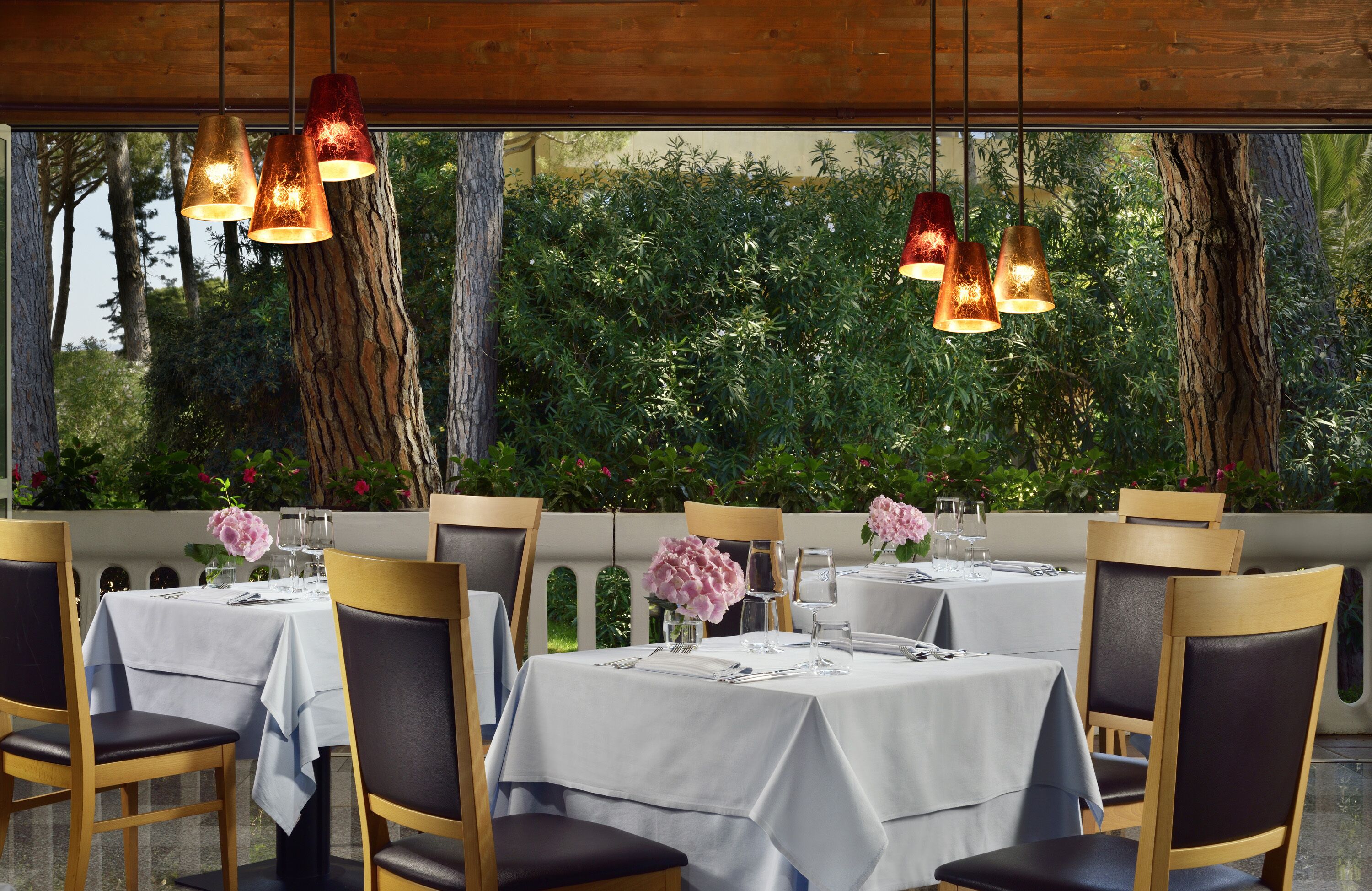 A restaurant with tables set for dining, wooden chairs, and hanging pendant lights.