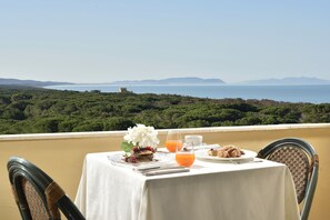 Una mesa preparada para el desayuno con una vista panorámica del mar y las colinas.