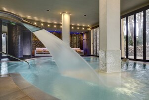 Una piscina interior moderna con tobogán de agua, zona de descanso con sofá y ventanas amplias que ofrecen vistas al exterior.