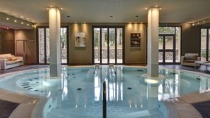 Una amplia piscina cubierta con agua cristalina, rodeada de tumbonas y un muro de piedra.
