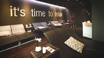 Ein moderner Entspannungsbereich mit verschiedenen Sitzgelegenheiten, darunter Sofas und ein Liegesessel, in einem großzügigen Raum, an dessen Wand der Schriftzug „Zeit zu entspannen“ angebracht ist.