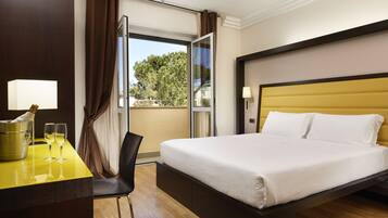 Una habitación de hotel con cama, escritorio con lámpara, silla y ventana con cortinas.