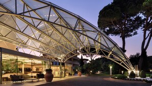 Un edificio moderno con una gran estructura de vidrio y metal, asientos exteriores y plantas en macetas.