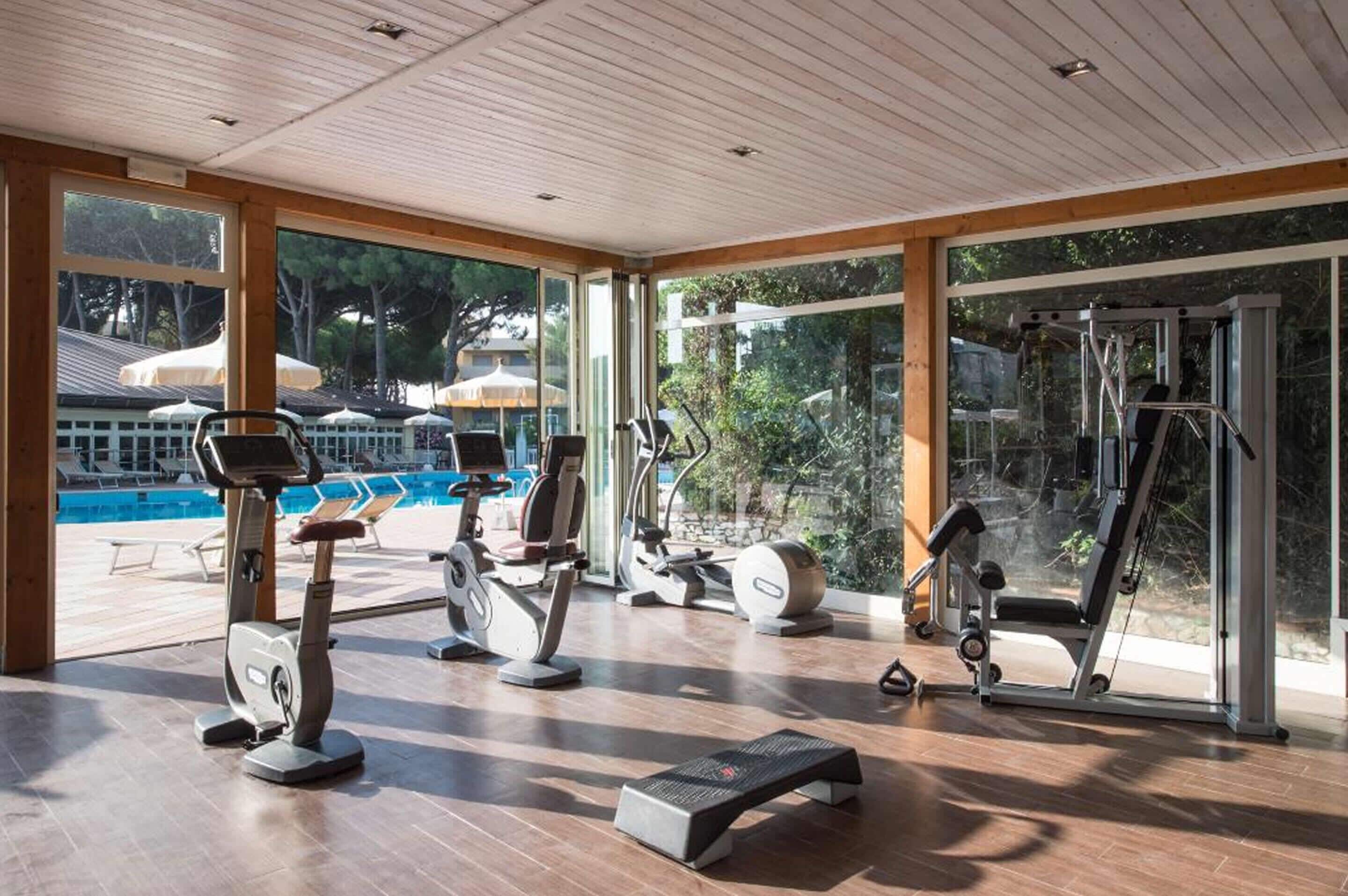 A gym with cardio machines, a step platform, and a view of a swimming pool and outdoor area.