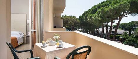 A balcony with a table set for two, chairs, and a view of a bedroom with a bed and a window.