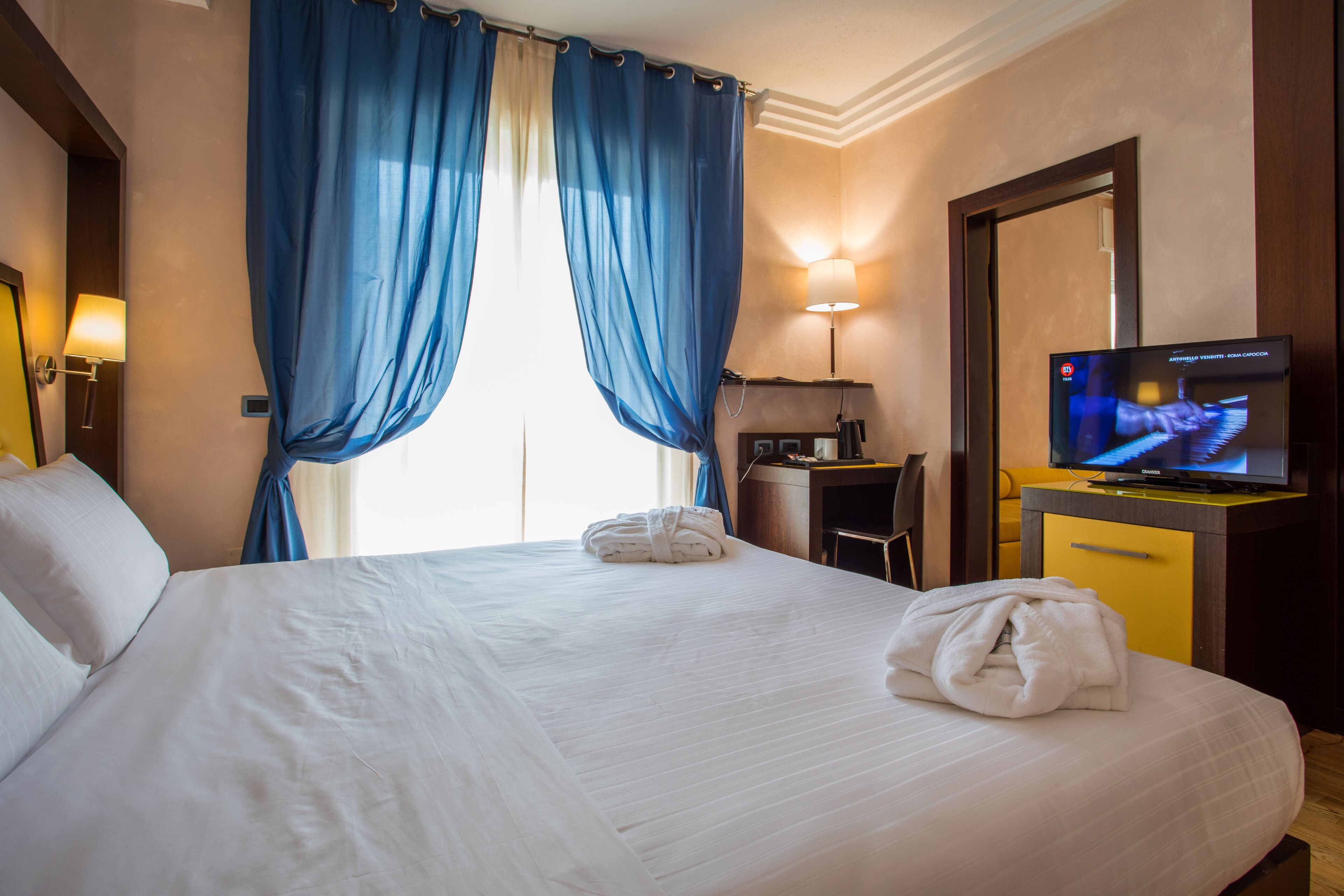 Een hotelkamer met een groot bed, een bureau met stoel, een televisie en een spiegel.